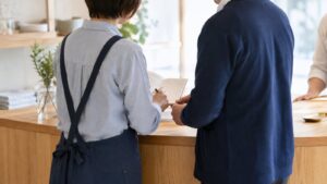 店舗のカウンターで、従業員と経営者が対応ノートを一緒に確認する様子